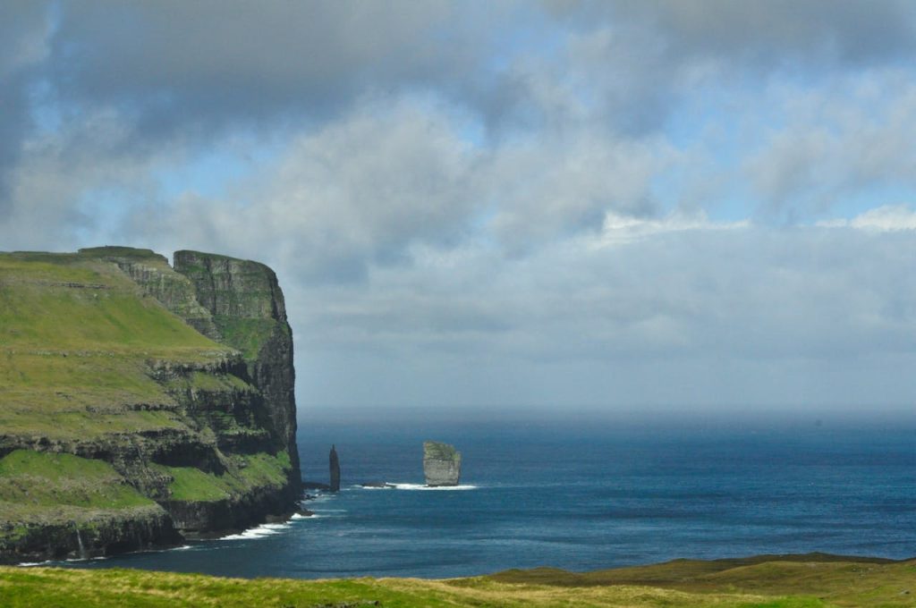 Majestic cliffs and sea stacks on the Faroe Islands under a cloudy sky, showcasing natures grandeur.