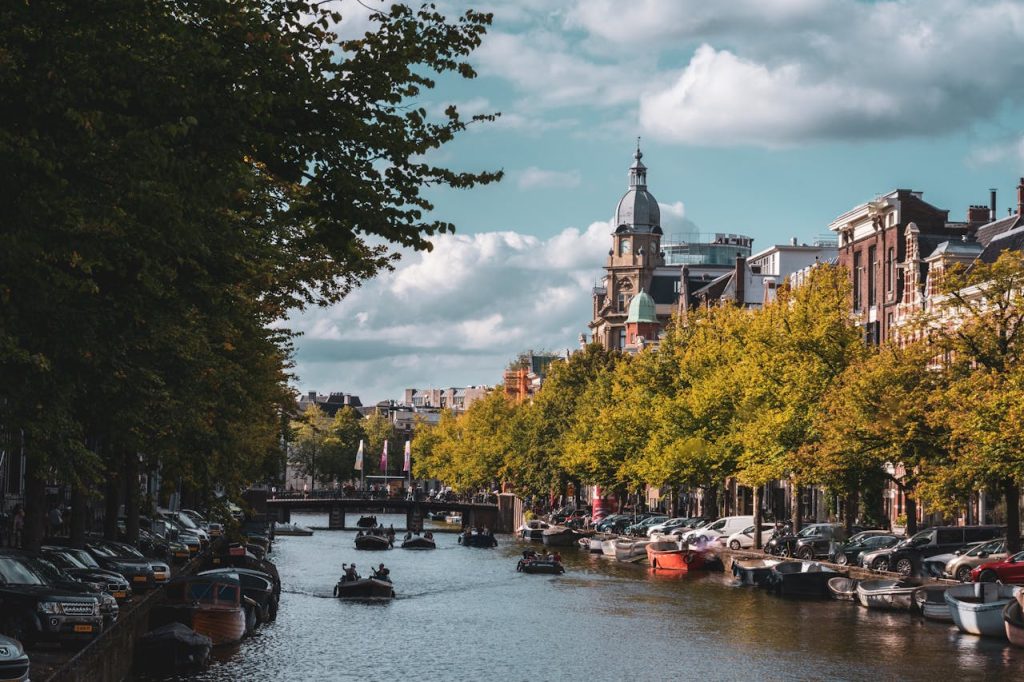 Experience the charming canals of Amsterdam adorned with vibrant trees and classic architecture.